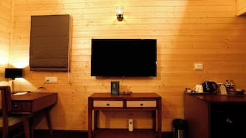 A wooden-paneled room with a television mounted on the wall, a desk with a lamp, and a small cabinet with various items on top.