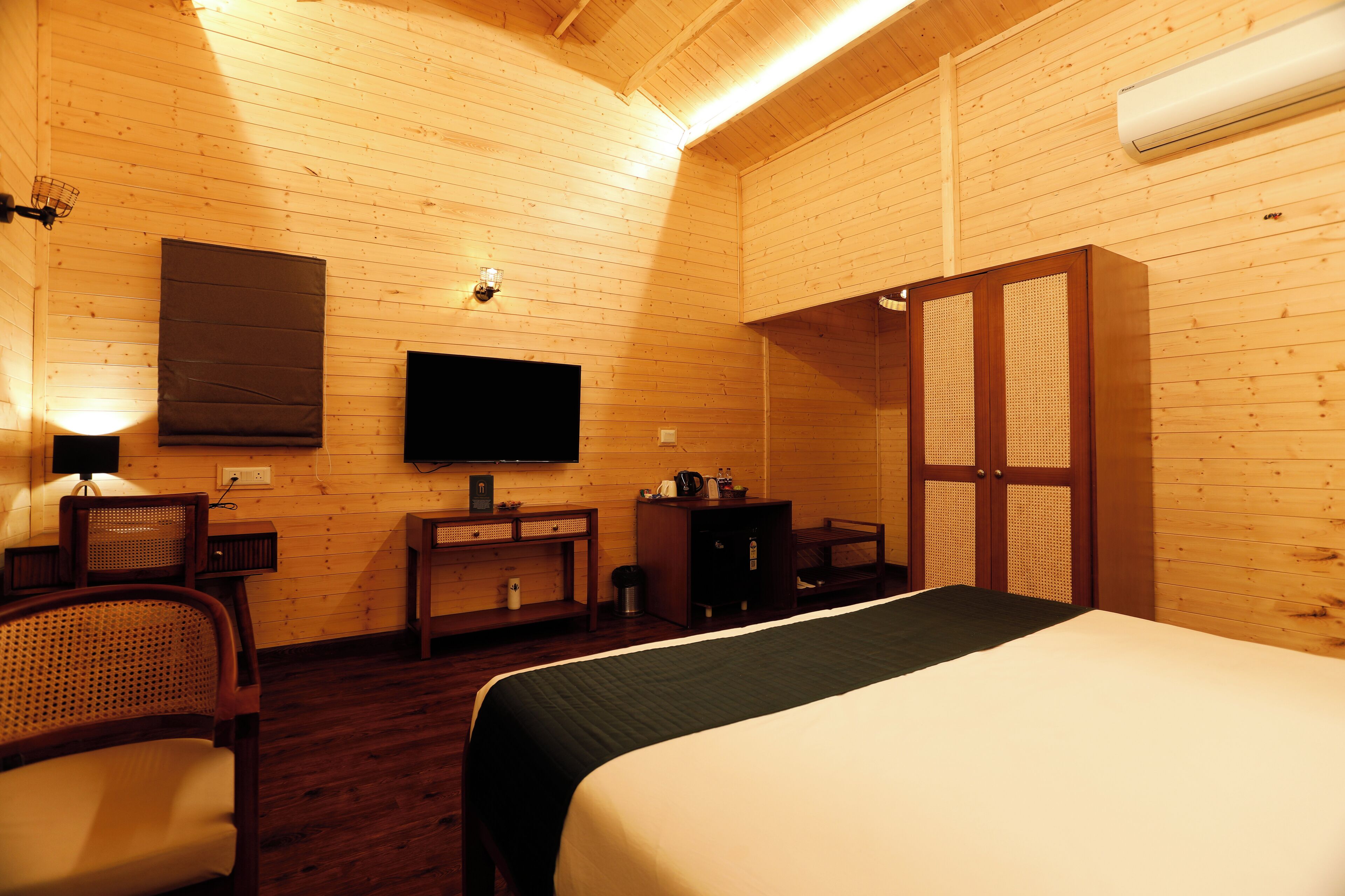 A wooden-paneled room with a bed, a television, a desk, and a wardrobe.