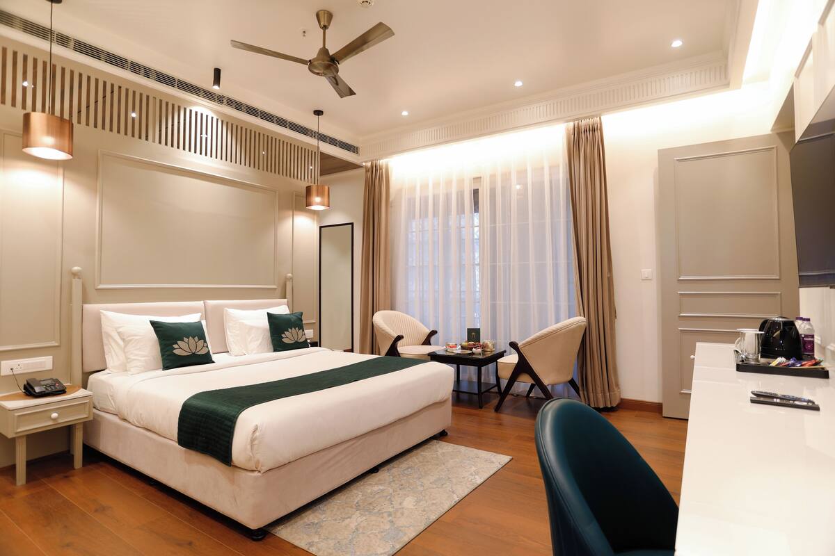 A modern hotel room with a large bed, a desk, and a chair. There is a ceiling fan, a window with curtains, and a nightstand with a phone.