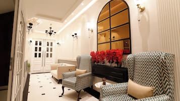 A hallway with a patterned floor, a piano, and two patterned armchairs with a vase of red flowers.