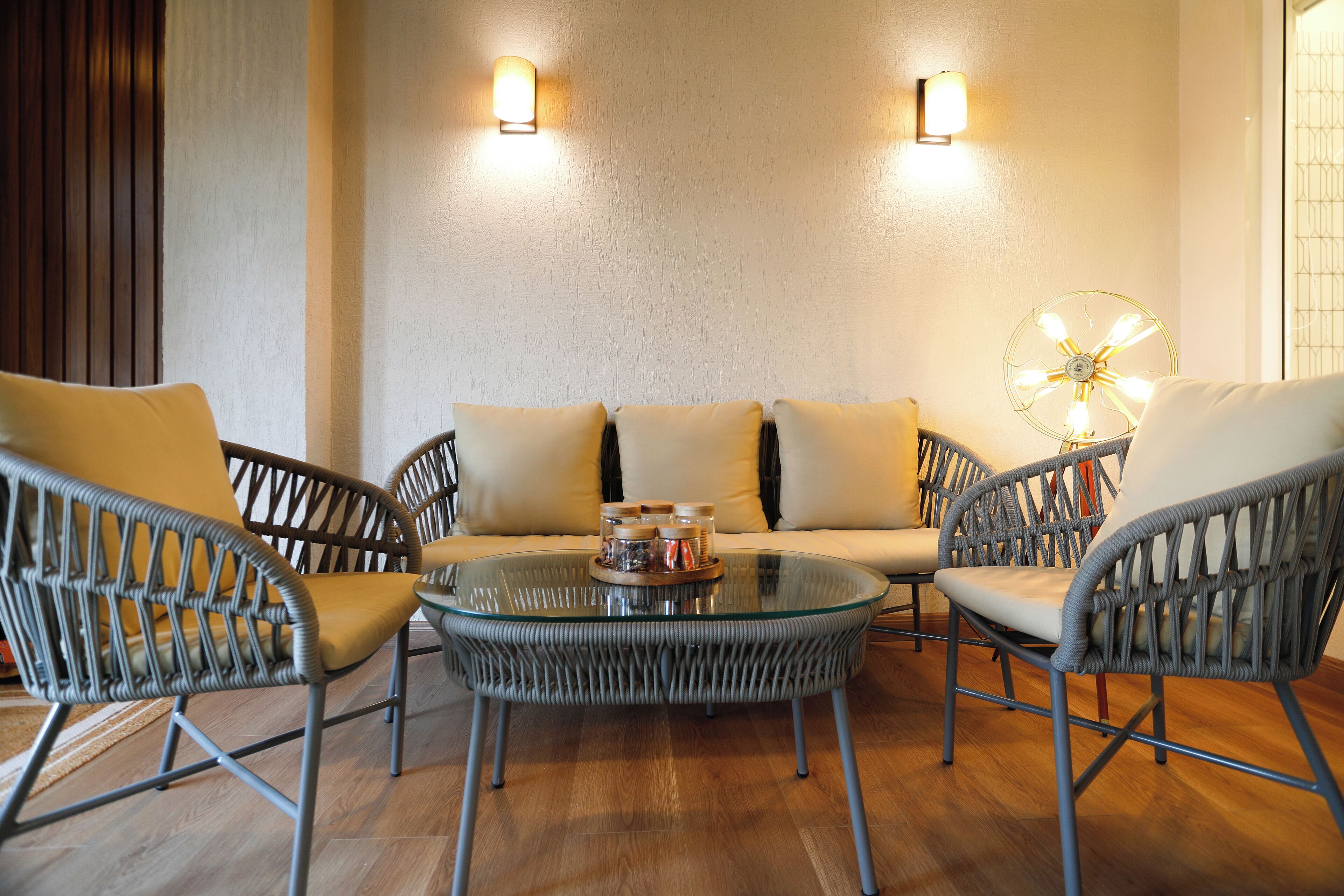 A modern lounge area with wicker furniture, a glass coffee table, and wall-mounted lights.