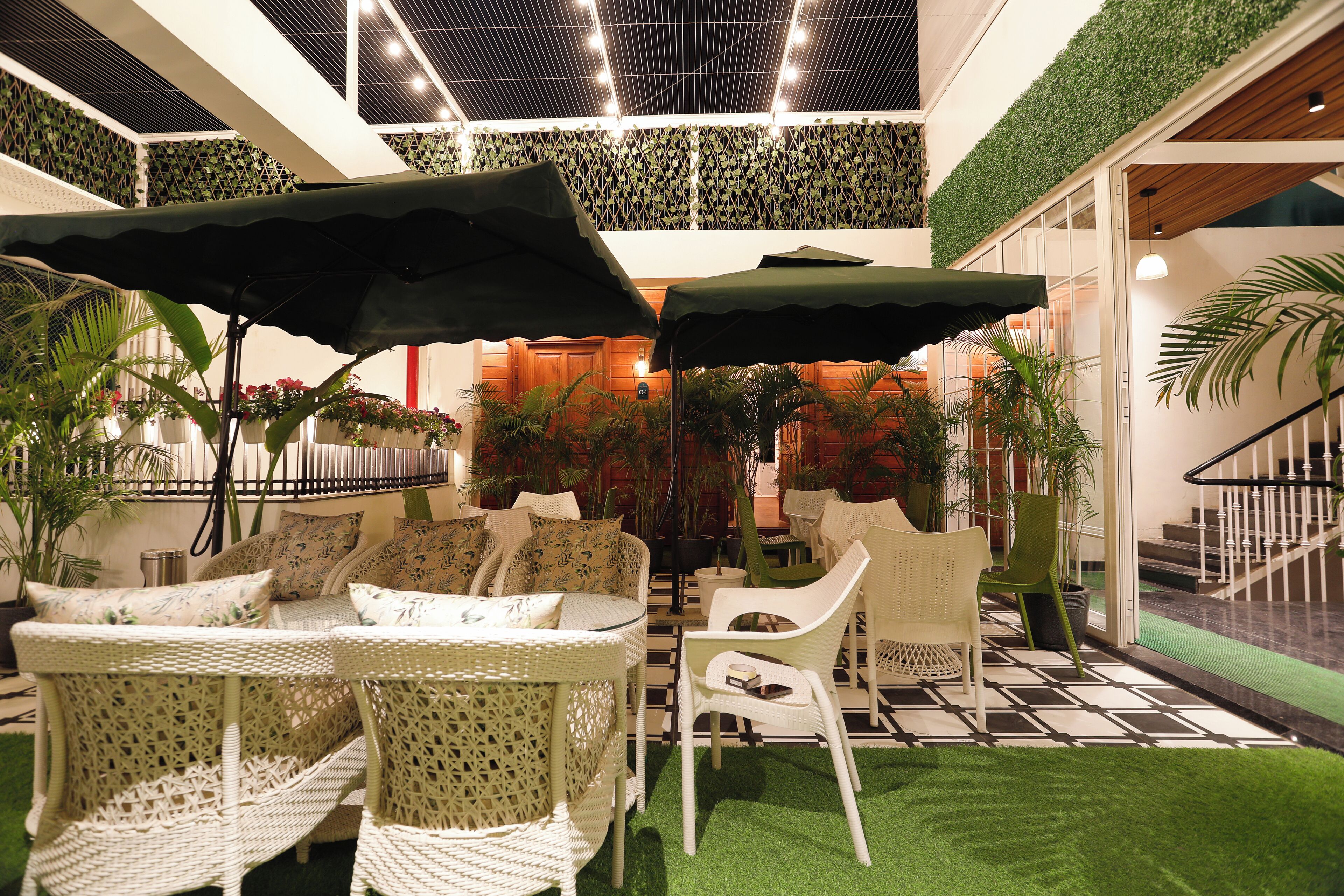 Ein überdachter Patio-Bereich mit Korbmöbeln, künstlichem Rasen in Grün und Blumentöpfen.