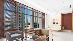 A modern hotel room with a large window, a sofa, a dining table, and a wooden partition.