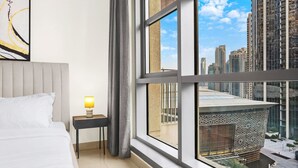 A hotel room with a bed, a bedside table with a lamp, a large window with a city view, and a modern architectural design.