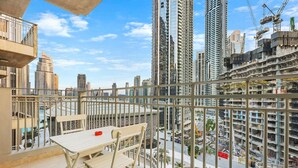 A balcony with a table and chairs overlooking a cityscape with high-rise buildings and construction cranes.