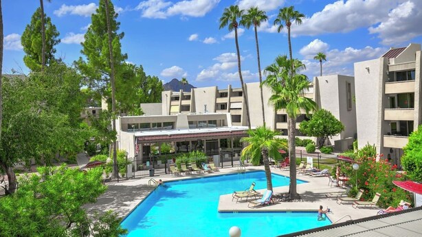 Un hotel con piscina rodeado de palmeras y una montaña al fondo.