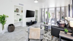 Una sala de estar moderna con una televisión de pantalla plana, un sofá, una mesa de centro y un amplio ventanal con cortinas.