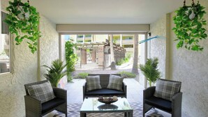 Un patio acogedor con mobiliario de mimbre, una mesa de centro de vidrio y plantas colgantes.
