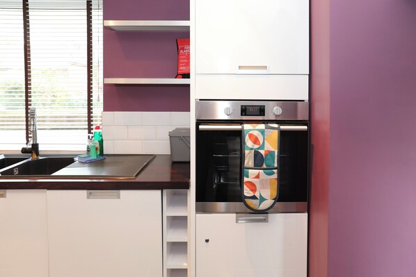 A kitchen with white cabinets, a stainless steel oven, and a colorful kettle hanging on the wall.