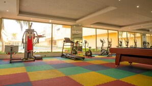 Un gimnasio con diverso equipo de ejercicio, piso de colores y ventanas amplias con vistas al exterior.
