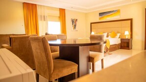 Habitación de hotel con una mesa de comedor redonda, asientos cómodos, una cama con cabecera y un cuadro en la pared.