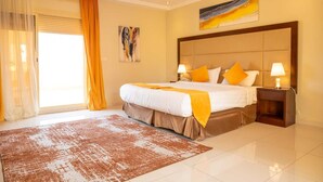 Habitación de hotel con una cama grande, dos mesitas de noche con lámparas, un amplio ventanal con cortinas y un cuadro en la pared.