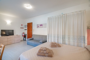 A hotel room with a bed, a sofa, a TV, a fire extinguisher, and a curtain. - Studio's Pavese (Olbia)
