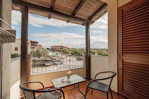A balcony with a table and chairs, a view of a street with cars, and buildings in the distance. - Studio's Pavese (Olbia)
