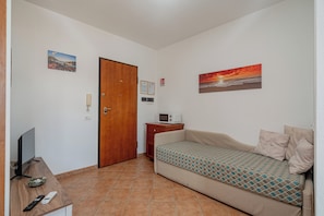 A small, compact room with a sofa, a television, a wooden door, and a small table with a microwave. - Studio's Pavese (Olbia)