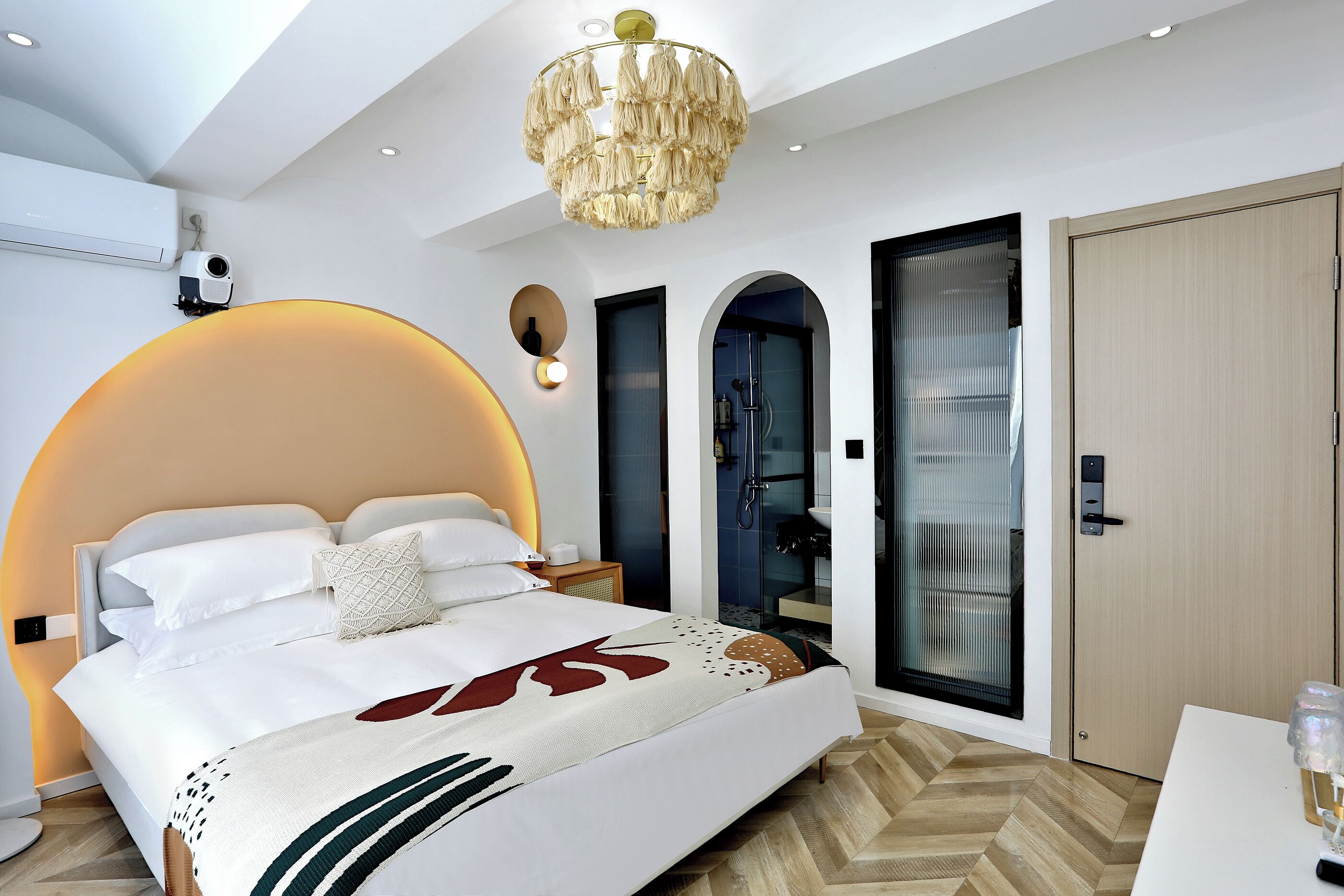 A modern hotel room with a large bed, a chandelier, a shower, and a wardrobe.