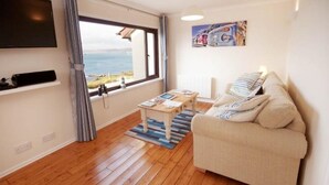 Un salon avec un canapé, une table basse, un téléviseur et une fenêtre donnant sur la mer.