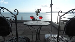 Une table avec deux verres à vin et un arrangement floral, donnant sur une étendue d’eau.