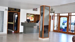 A reception area with a sign for 'MADHU BAN Restaurant', a reception desk, a large glass partition, and a view of the outside through large windows. - HOTEL TRIDEV  (Reasi)
