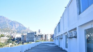A rooftop terrace with a view of a cityscape and mountains in the distance. - HOTEL TRIDEV  (Reasi)