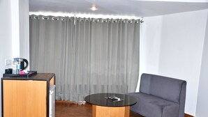 A room with a round wooden table, a grey sofa, a wooden cabinet, and a curtain. - HOTEL TRIDEV  (Reasi)