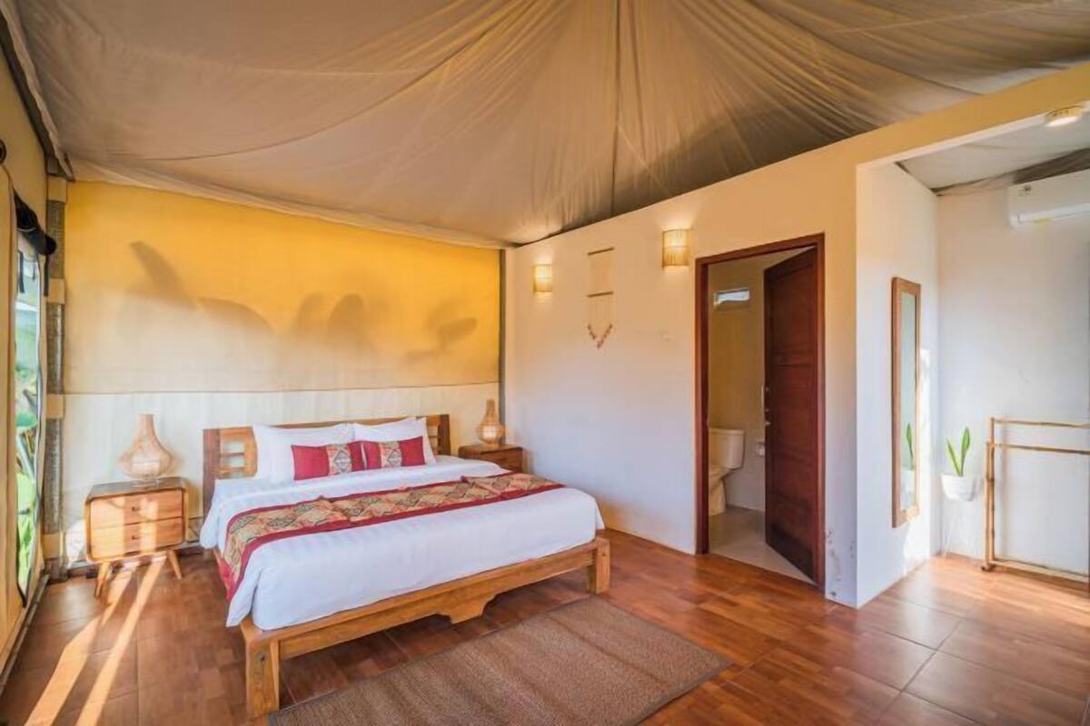 Un dormitorio con cama de madera, un ventanal grande y una puerta que da a otra habitación.