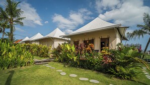 A row of white tents with a well-maintained garden in front, including a stone path and tropical plants. - Paddy's Glamping (Munggu)