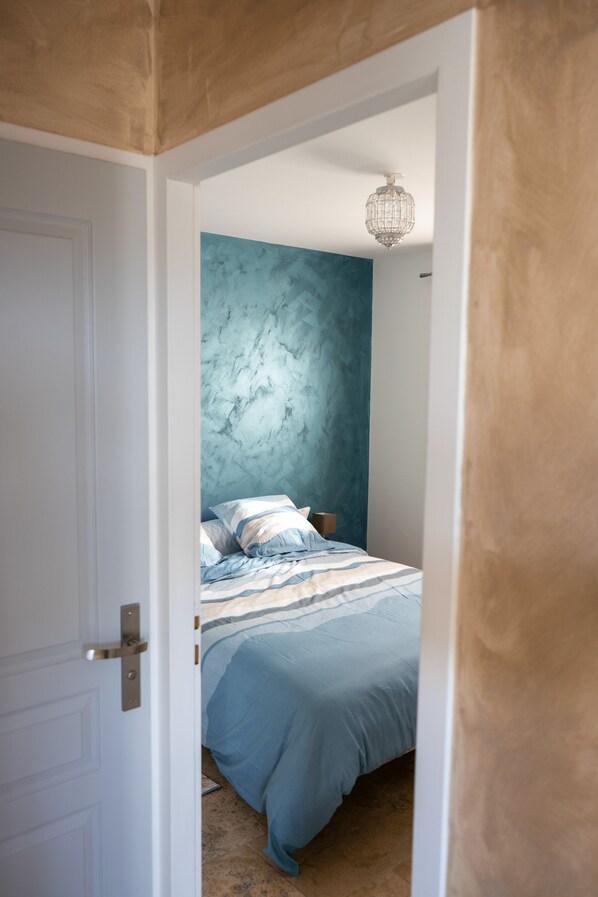 A bedroom with a bed, a door, and a wall with a textured pattern. - An Oasis of Peace Near Avignon (Sorgues)