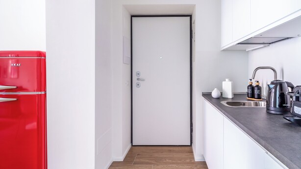 Una cocina moderna con un refrigerador rojo, una puerta blanca y una encimera con un hervidor y dispensador de jabón.