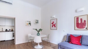 Una sala de estar moderna con un sofá gris, una mesa de centro blanca y un comedor con una mesa y sillas blancas.