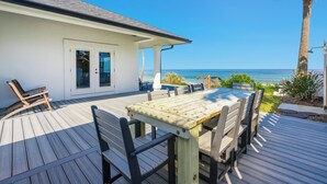 Eine Terrasse mit Holztisch und -stühlen mit Blick auf einen Strand.