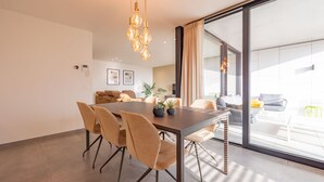 A modern dining area with a long table, multiple chairs, and pendant lighting. - Apartment in Nieuwpoort With Balcony (Nieuwpoort)