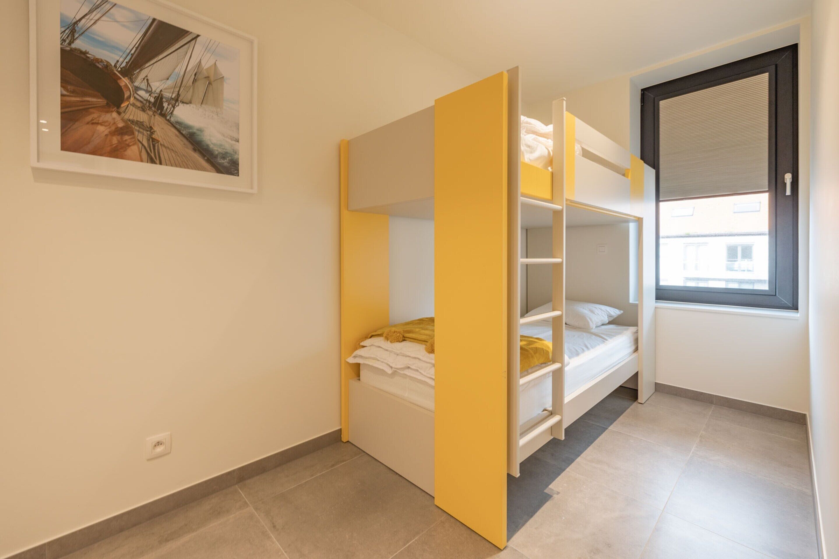 A compact room with a bunk bed, a window with blinds, and a framed picture on the wall.