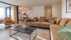 A modern living room with a sofa, armchair, and coffee table. There is a dining area with chairs and a table in the background. - Apartment in Nieuwpoort With Balcony (Nieuwpoort)