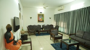 A living room with a sofa, armchairs, a coffee table, a TV, and a statue. - Heritage Garden Villa (Mangaluru)