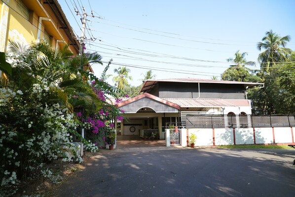 A two-story building with a covered entrance, a gated driveway, and lush greenery including flowering plants and palm trees. - Heritage Garden Villa (Mangaluru)