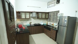 A kitchen with dark wooden cabinets, a stainless steel refrigerator, and a gas stove. - Heritage Garden Villa (Mangaluru)
