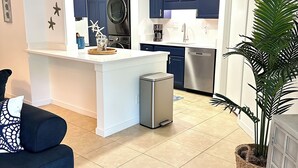 A modern kitchen with a central island, built-in appliances, and a dining area with a blue sofa. - Beautiful Forest Beach Villas couple's retreat. 5 min walk to Coligny Beach (Hilton Head Island)