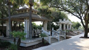 A gazebo with a wooden deck, surrounded by palm trees and a white fence. - Beautiful Forest Beach Villas couple's retreat. 5 min walk to Coligny Beach (Hilton Head Island)