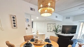 A dining area with a round table, wicker chairs, a woven light fixture, and a television in the background. - Beautiful Forest Beach Villas couple's retreat. 5 min walk to Coligny Beach (Hilton Head Island)