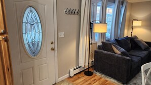 Une pièce avec une porte blanche ornée d’un vitrail, un canapé gris foncé, un lampadaire et un porte-manteau.
