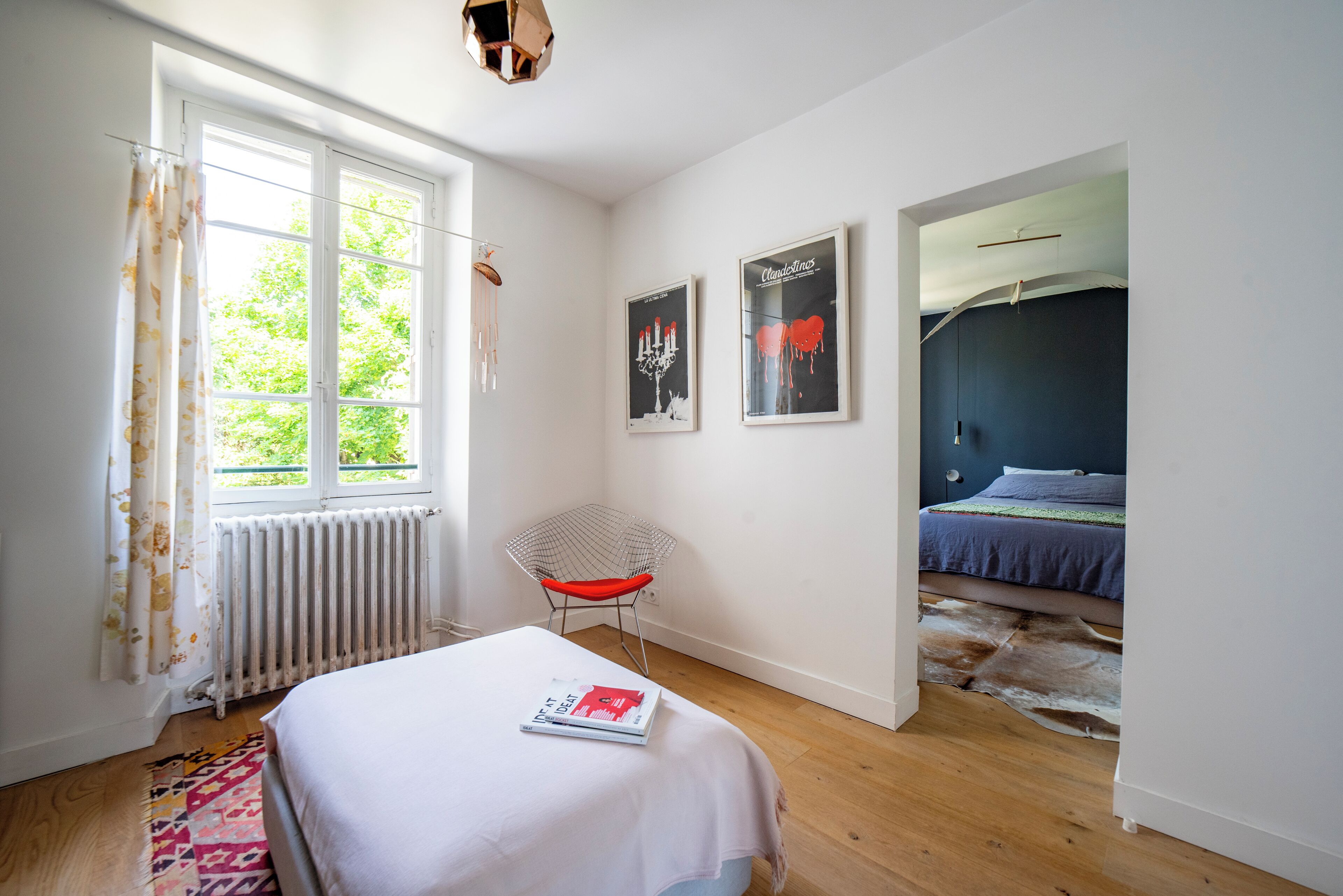 Ein Schlafzimmer mit einem Bett, einem Sessel, einem Heizkörper, einem Fenster und zwei gerahmten Bildern an der Wand.