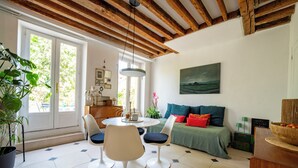 Une pièce avec un plafond en bois, un canapé vert, une table blanche avec des chaises et une grande fenêtre.