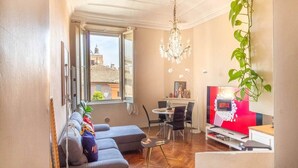 A living room with a sofa, a dining area with chairs, a chandelier, a plant, and a Netflix sign. - Canalchiaro Suite, 6 guests (Modena)
