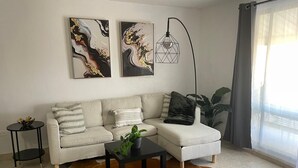 Una sala de estar moderna con un sofá, una mesa de centro, una mesita auxiliar y un tapiz de cuero de vaca. Hay dos cuadros abstractos en la pared y una lámpara de pie.