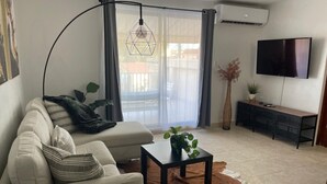 Una sala de estar moderna con un sofá, una mesa de centro, un televisor y un ventanal con cortinas.