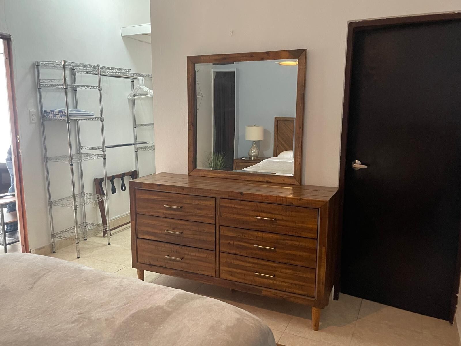 Une chambre à coucher avec une commode en bois, un miroir et une étagère en métal.