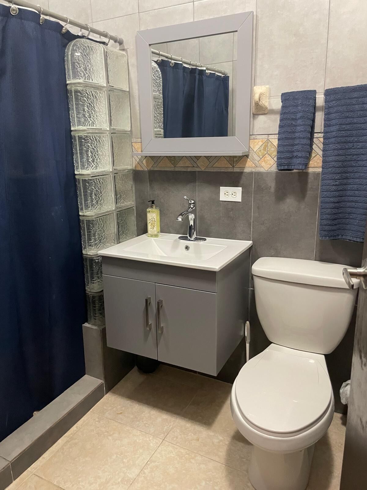 A bathroom with a glass shower enclosure, a white sink with a mirror above it, and a toilet.
