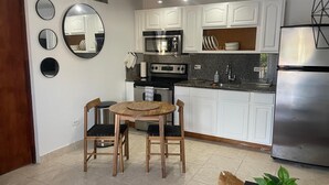 Una cocina moderna con armarios blancos, un refrigerador de acero inoxidable, un microondas y una estufa. Hay una mesa de comedor con dos sillas y una alfombra pequeña.