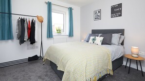 A bedroom with a bed, a bedside table, a radiator, a window with curtains, and a wall with two framed pictures. - 3 Bedroom Large House - Train Station (Derby)